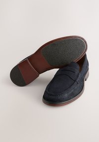 Marineblaue Wildleder-Slipper mit Mokassin-Design, gesteppten Details, einer braunen Ledersohle und einem strukturierten schwarzen Gummimantel für besseren Halt.