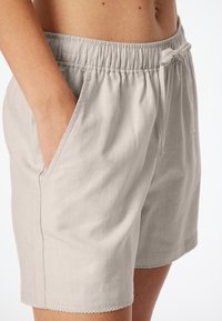 Ljusbeiga shorts gjorda av mjukt stoff med resårmidja och dragsko. Har fickor med lappar och en scalloped nederdel.