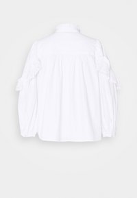 Blouse en coton blanc avec manches longues bouffantes, col à volants et détails en dentelle ajourée sur les manches. Texture lisse et coupe décontractée.