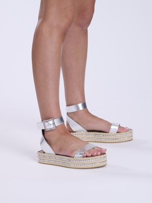 Sandales espadrilles métalliques argentées avec semelles plates, brides de cheville avec boucles décoratives et détails en jute tissé contrastants.