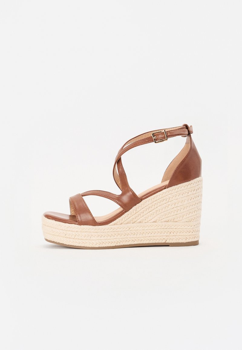Sandale compensée en cuir marron avec bride à boucle à la cheville et talon plateforme en jute tressée sur fond blanc.