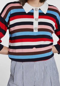 Kleurrijke gestreepte trui in donkerblauw, rood, roze, bruin en witte tinten. Heeft een witte kraag en knopen met edelsteenaccenten aan de voorkant.