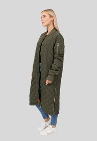 Pikowany oliwkowo-zielony długi płaszcz z zamkiem błyskawicznym z przodu, ściągany na mankiety i z bocznymi suwakami. Połączony z jeansami i białymi trampkami.