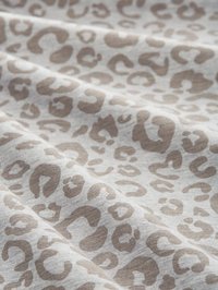 Lätt tyg med ett beige leopardmönster på en mjuk grå bakgrund, med slät textur och subtil glans.
