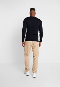 Marineblauwe gebreide trui met lange mouwen, gecombineerd met lichtbeige corduroy broek en witte sneakers. De textuur is glad en de pasvorm is casual.