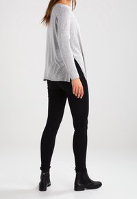 Maglione grigio a maniche lunghe con vestibilità rilassata e spacco laterale, abbinato a jeans skinny neri e stivaletti. Texture liscia, design casual.