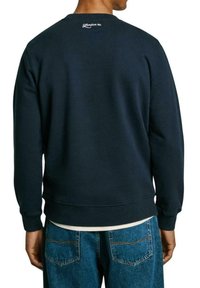 Felpa blu navy realizzata in tessuto morbido, con collo rotondo, polsini e orlo a costine, e con un logo sulla parte posteriore vicino al collo.