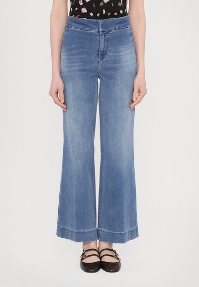 Jeans din denim cu picioare largi, de culoare albastră deschisă, având talie înaltă, un finisaj curat și o margine ușor desfăcută la gleznă. Textură netedă.
