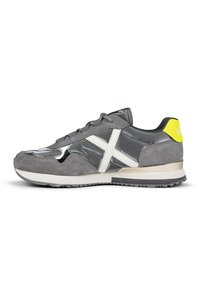 Gray athletic shoe made of suede and synthetic materials. Features a white cross design, metallic accents, and a textured sole.