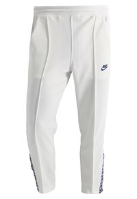 Vitaid sportbyxor i vitt med en slät textur, med en blå Nike-logotyp och mönstrade sidodetaljer i röd och blå.