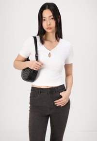 Top bianco a coste con dettagli a chiave nel collo, abbinato a jeans neri a vita alta e una borsa rotonda nera con borchie.