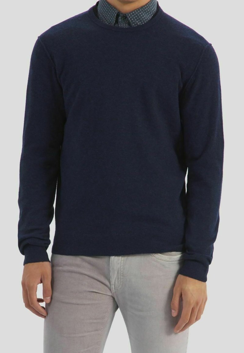 Donkerblauwe crewneck sweater gemaakt van zachte gebreide stof. Bevat lange mouwen en een aansluitend ontwerp, gedragen over een gestreept overhemd met kraag.