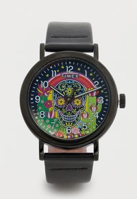 Montre Timex ronde avec un bracelet en cuir noir. Design vibrant de crâne sur le cadran, avec des motifs floraux et des éléments colorés sur un fond sombre.