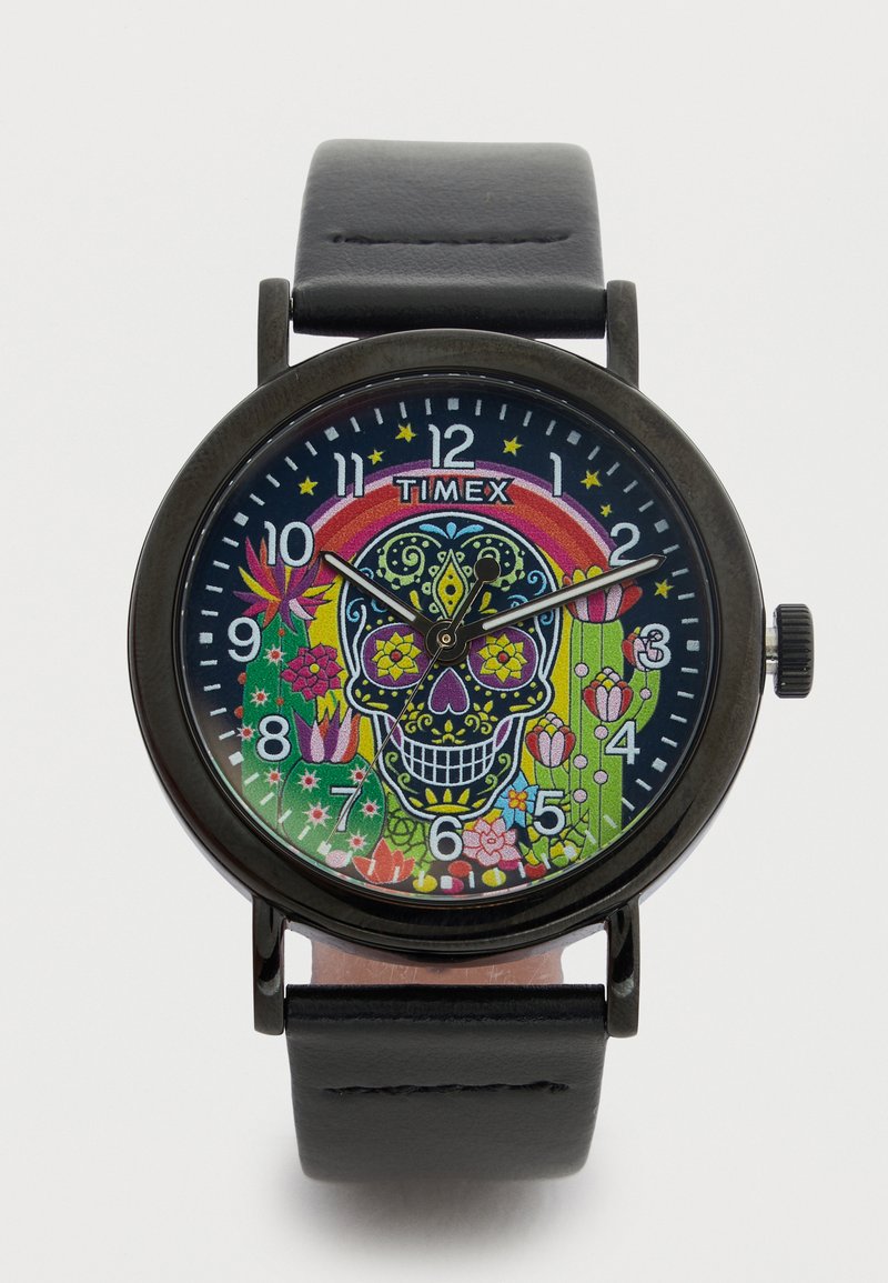 Montre Timex ronde avec un bracelet en cuir noir. Design vibrant de crâne sur le cadran, avec des motifs floraux et des éléments colorés sur un fond sombre.
