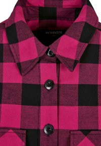 Camisa de franela a cuadros pink y negra con un clásico cuello extendido, botones negros y un detalle de bolsillo frontal. Textura suave, diseño entallado.