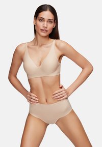 Sujetador sin costuras en tono nude con tirantes anchos y diseño en forma de v, combinado con braguitas de talle alto sin costuras a juego. Textura suave, silueta ajustada.