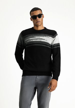 Suéter de punto negro con rayas horizontales en tonos de gris. Puños y dobladillo acanalados. Modelo usando gafas de sol, posando frente a un fondo liso.