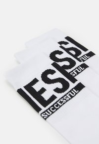 Hvide sokker med sort tekst, med ordet "SUCCESSFUL" i fed sort skrift øverst og ribbede manchetter.