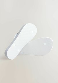 Baltos gumos šlepetės su tekstūruotais padais, turinčios lygias kraštus ir ventiliacijos angas. Dizainas yra minimalistinis, be matomų raštų.