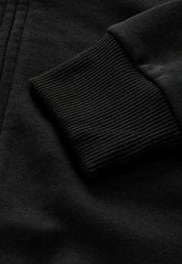 Tissu de sweat-shirt noir avec un gros plan d'un poignet côtelé, présentant une texture lisse et une couleur uniforme.