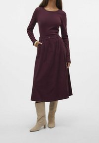 Pitkä, tummanpunainen hame, jossa on laskokset, yhdistettynä sopivaan paitaan. Yhdistettynä vaaleanbeigeihin polviin ulottuviin korkokenkiin. Sileä pinta ja muotoiltu malli.