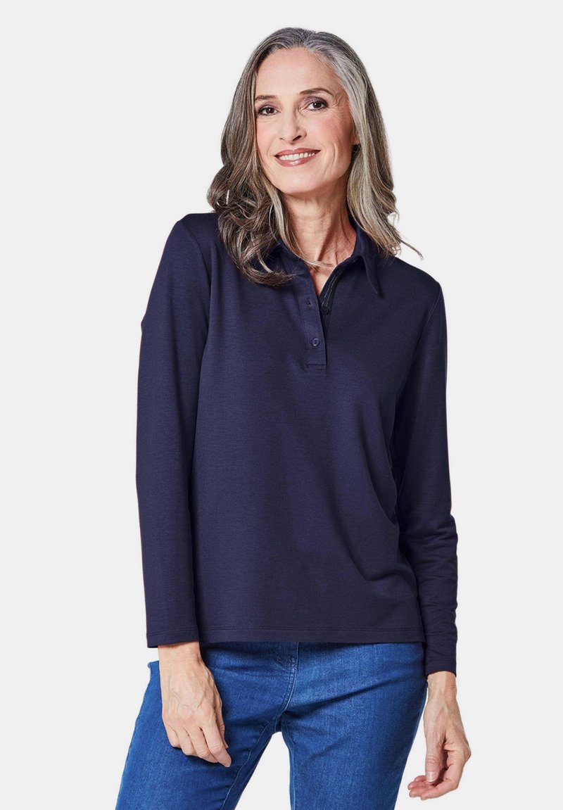 Marineblaues Langarm-Polohemd mit Kragen und Knopfleiste. Das Material wirkt glatt und leicht und wird mit einer blauen Jeans kombiniert.