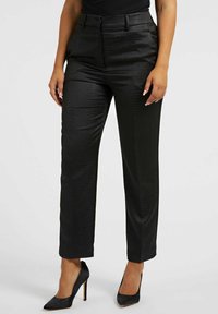 Pantalon noir avec un motif texturé de peau de reptile, coupe droite et taille haute. Associé à des talons hauts noirs étincelants.