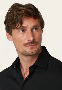 Schwarzes Hemd mit Kragen und weichem Griff. Verfügt über ein Knopfverschluss-Design, glatte Stoffqualität und einen klassischen Kragen. Nahaufnahme des Kragenbereichs.