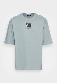 T-shirt en coton bleu ciel avec des manches courtes, un col rond et un design d'étiquette graphique imprimé sur le devant. Texture lisse.