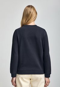 Felpa navy realizzata in morbido tessuto uniforme, con scollo a girocollo e polsini a costine, mostrata dalla schiena con un design semplice.