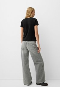 Black short-sleeve top paired with loose, light gray wide-leg jeans. The jeans feature back pockets and a faded texture.