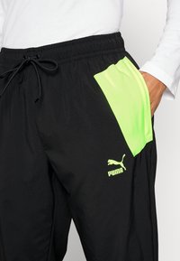 Schwarze Sporthose mit einer neongrünen Seitentasche und Logo. Verfügt über einen Kordelzugbund und ein glattes, leichtes Material.