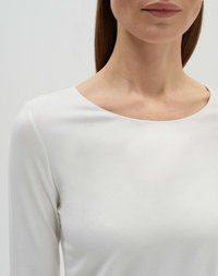 Haut blanc à manches longues avec un col bateau, texture douce et tissu lisse. Vue en gros plan se concentrant sur la partie supérieure du corps.