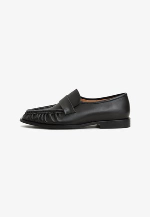 Black leather loafers with a rounded toe, gathered detailing on the front, and a flat sole. Minimalistic design with smooth texture.