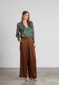 blusa floral en color azul verdoso con cuello de solapa, combinada con pantalones de pierna ancha de satén marrón; ambos tejidos parecen suaves y livianos.