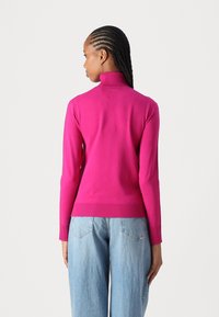 Hooggesloten pullover in opvallend roze breimateriaal, met lange mouwen en ribgebreide boorden en zoom, gecombineerd met losse blauwe spijkerbroek.
