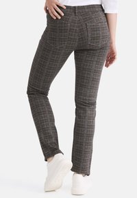 Graue karierte Hose im Slim-Fit mit Gesäßtaschen und strukturiertem Stoff. Getragen mit weißen Sneakern.