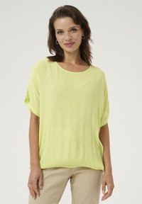 Blusa de manga corta color verde lima con un corte holgado, hecha de un tejido texturizado. Cuello redondeado y mangas relajadas, combinada con pantalones beige.