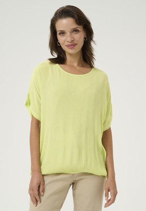 Haut vert citron à manches courtes avec une coupe ample, en tissu texturé. Encolure arrondie et manches détendues, associé à un pantalon beige.