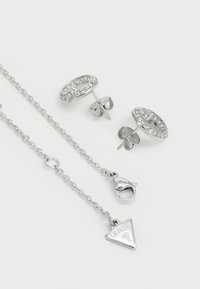 Zilverkleurige oorbellen met cirkelvormige vormen, versierd met heldere rhinestones; vergezeld van een zilveren ketting met een driehoekige hanger.