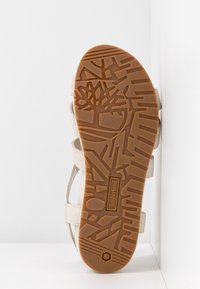 Semelle de sandale avec motifs géométriques et d’arbres, bande de roulement en caoutchouc brun clair et logo Timberland embossé au centre.
