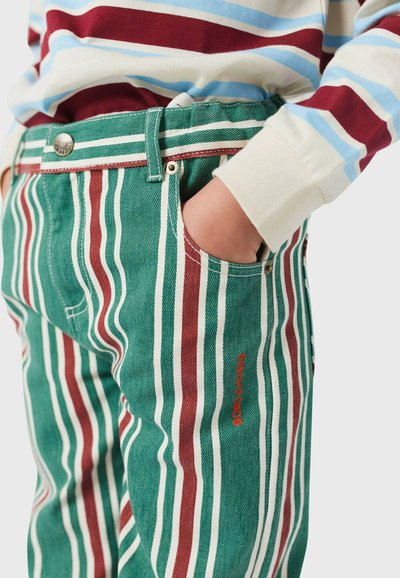 Pantalones de algodón a rayas con rayas verticales en verde, rojo y blanco. Cuentan con un cierre de botón en la cintura y un bolsillo frontal visible.