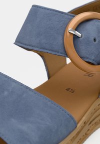 Μπλε πλατφόρμα σάνδαλο με φαρδιά λουριά και κυκλική πορτοκαλί αγκράφα, με υφή στην σόλα. Καφέ πάτος με σημάνσεις μεγέθους.