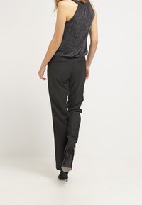 Czarne dopasowane spodnie o gładkiej fakturze, z wąskim krojem i tylnymi kieszeniami, zestawione z czarnymi szpilkami, widok z tyłu.