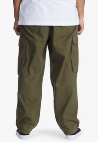 Khaki cargo kalhoty s bočními kapsami, volný střih a strukturovaná látka. Mají elastické manžety u kotníků a plochý pas.