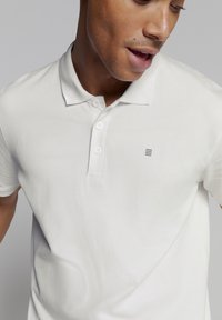 Witte polo shirt van gestructureerde stof, met een drie-knopen placket en een klein logo detail aan de linkerkant.
