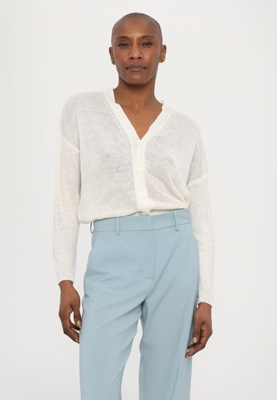 Cardigan ușor, din crem, cu decolteu în V, butoane frontale și mâneci lungi, asortat cu pantaloni tăiați de culoare albastru deschis. Textură netedă în general.