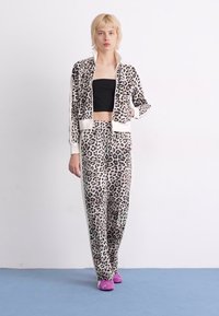 Leopard print tracksuit with a zip-up jacket and elastic waistband pants. Soft fabric, light beige background, black spots, and white accents.