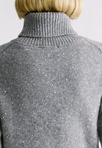 Grijze trui met een hoge ribbelkraag, voorzien van een gestructureerd oppervlak versierd met kleine sprankelende accenten. 'Pepe Jeans'-logo geborduurd op de achterkant.