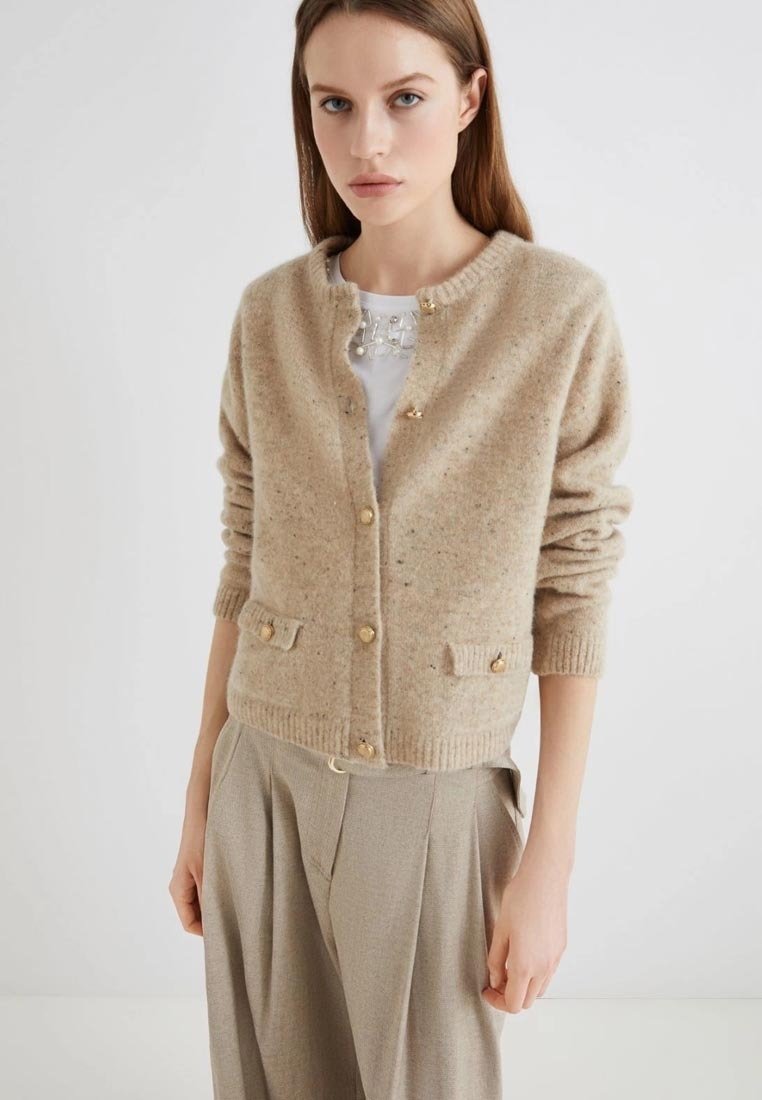 Cardigan in lana beige con collo rotondo, cinque bottoni dorati e due tasche frontali. La trama è morbida con un leggero motivo a macchie.